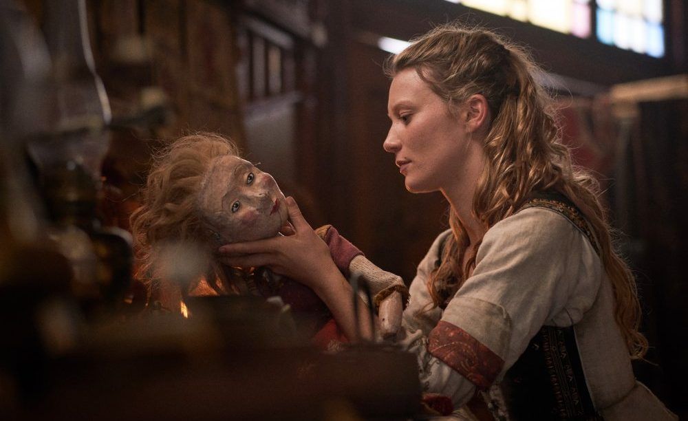 Mia Wasikowska in period costume tenderly holding a Judy puppet from a Punch and Judy show