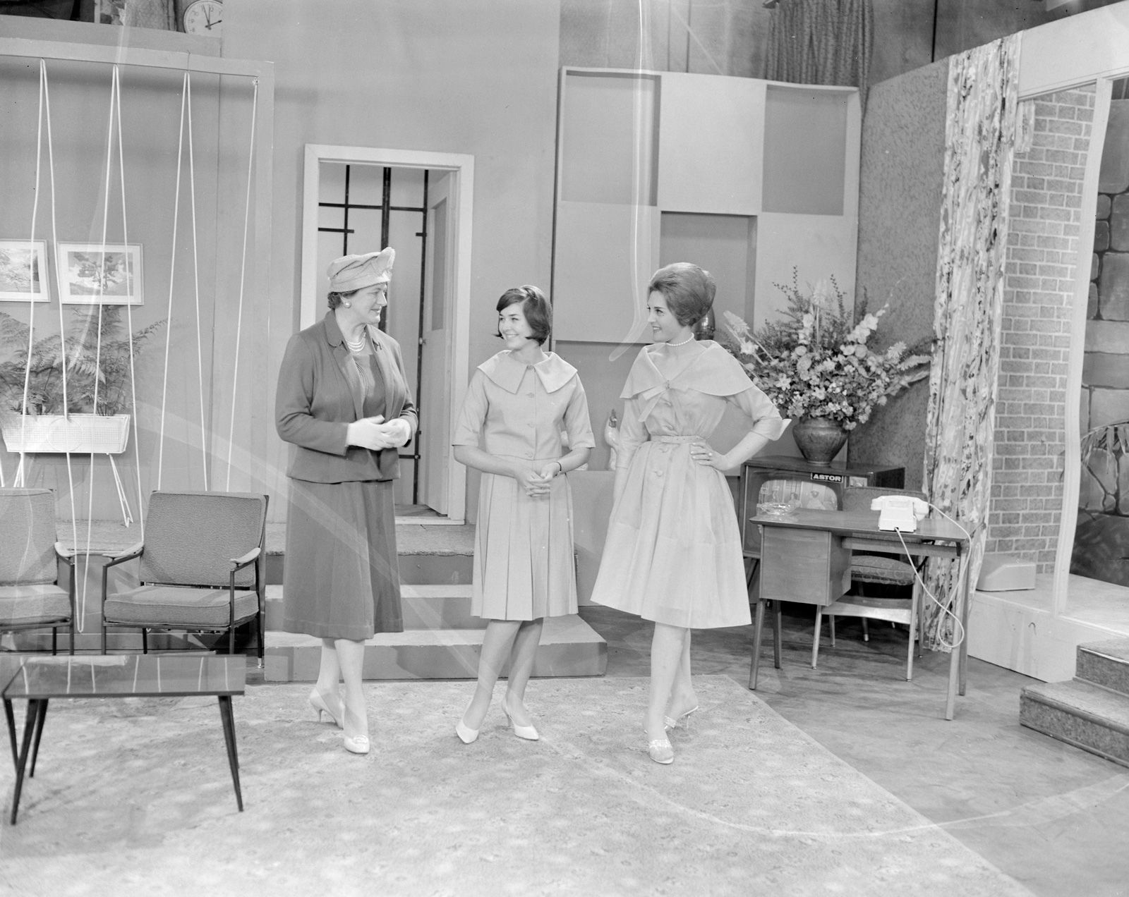 Three women standing in the middle of a television studio that is set to look like a suburban living room, c1960.