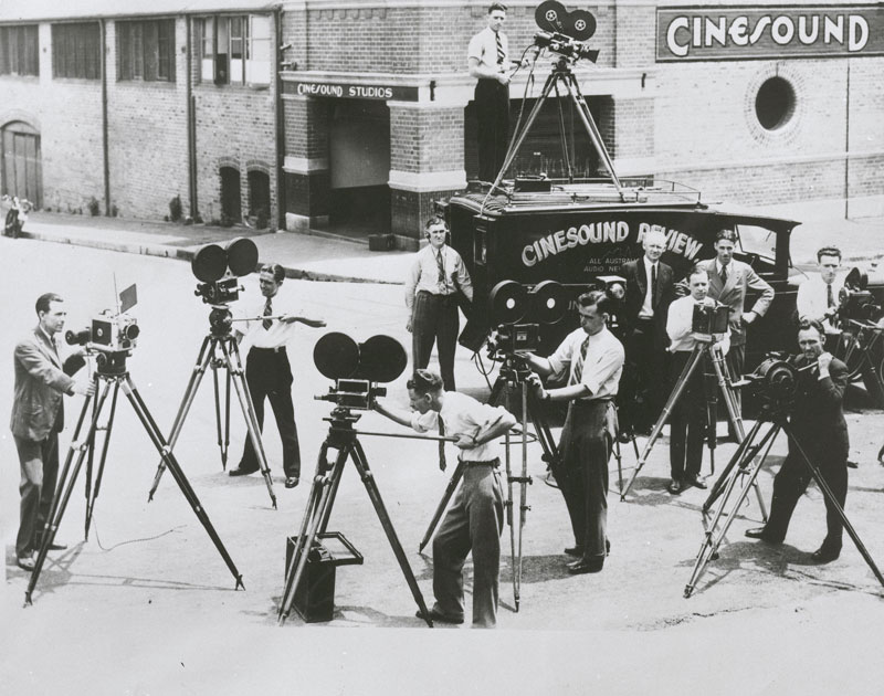 Shows the crew that captured the opening of the Sydney Harbour Bridge outside the Cinesound Productions studio.