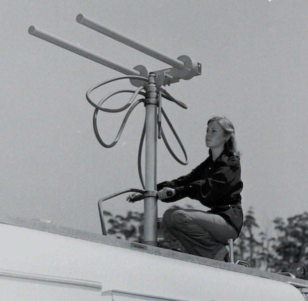 A woman is on the roof of a news cruiser van. She is operating a large metal technical instrument.