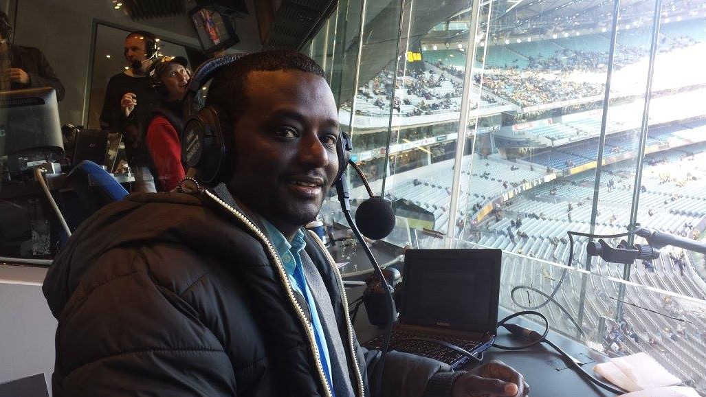 Man sits in the commentary box the the Melbourne Cricket Ground wearing headphones
