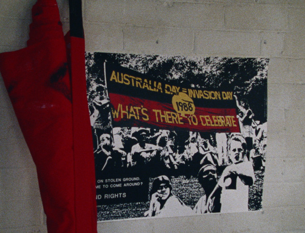 A sign on a wall featuring the Aboriginal flag that reads Australia Day = Invasion Day