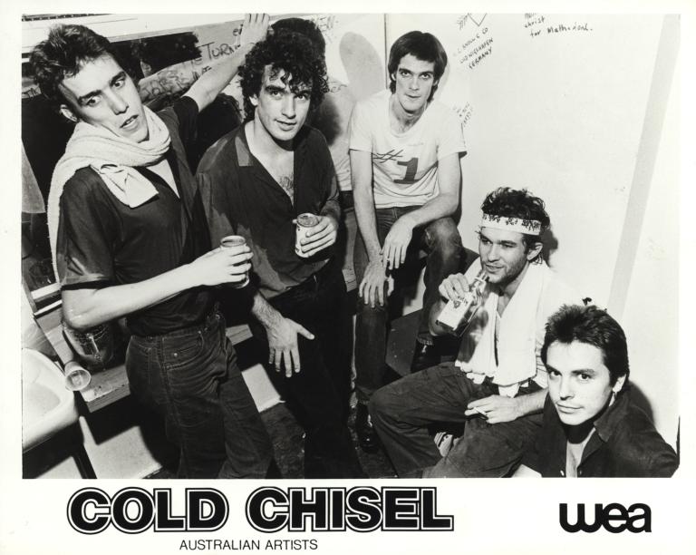 Members of rock band Cold Chisel in a graffitied room drinking beer and bourbon. Left to right: Steve Prestwich, Ian Moss, Don Walker, Jimmy Barnes, Phil Small.
