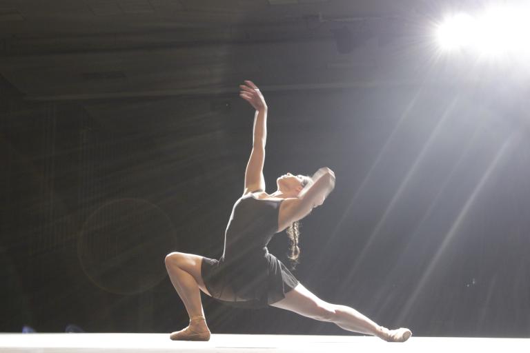 A dancer in a black dress poses on stage under a bright light
