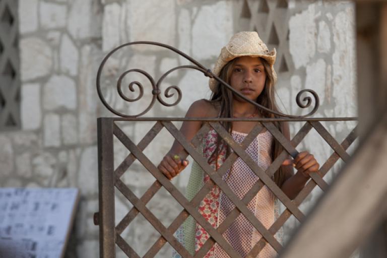 A young girl wearing a hat looking over an iron gate
