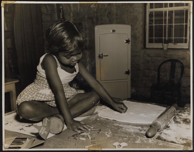 A small Aboriginal girl seated on a table playing.