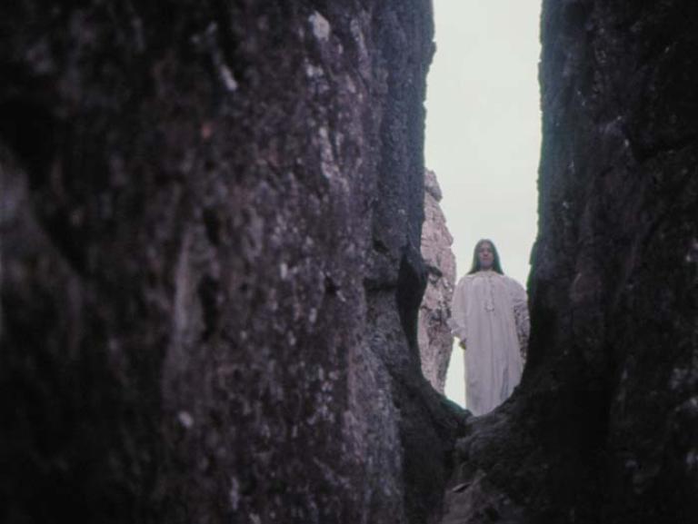 Sara in a white nightgown looks down from a crevice at Hanging Rock in a scene cut from Picnic at Hanging Rock.