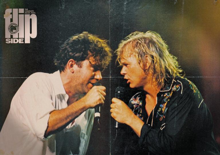  Head and shoulders image of Jimmy Barnes and John Farnham facing eachc other with microphones in their hands. Jimmy Barnes is dressed in a white shirt and John Farnham in a black embroidered shirt. Title of the magazine in white text at top.