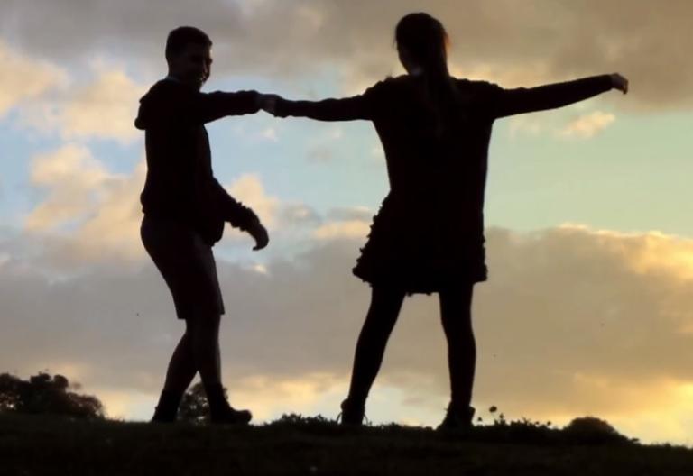 A silhouette of a boy and girl dancing in front of a sunset