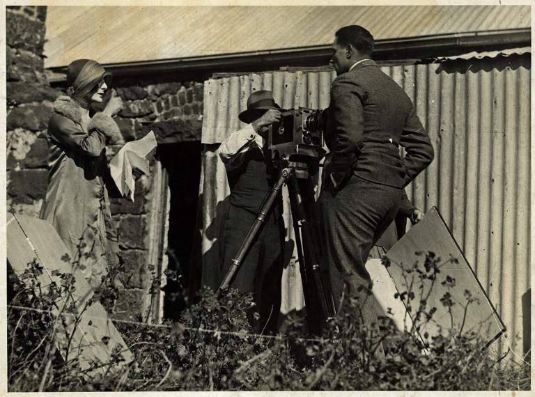 Paulette McDonagh directing a scene from the silent film The Far Paradise outside an old shed. You can also see a camera man and the lead actor.