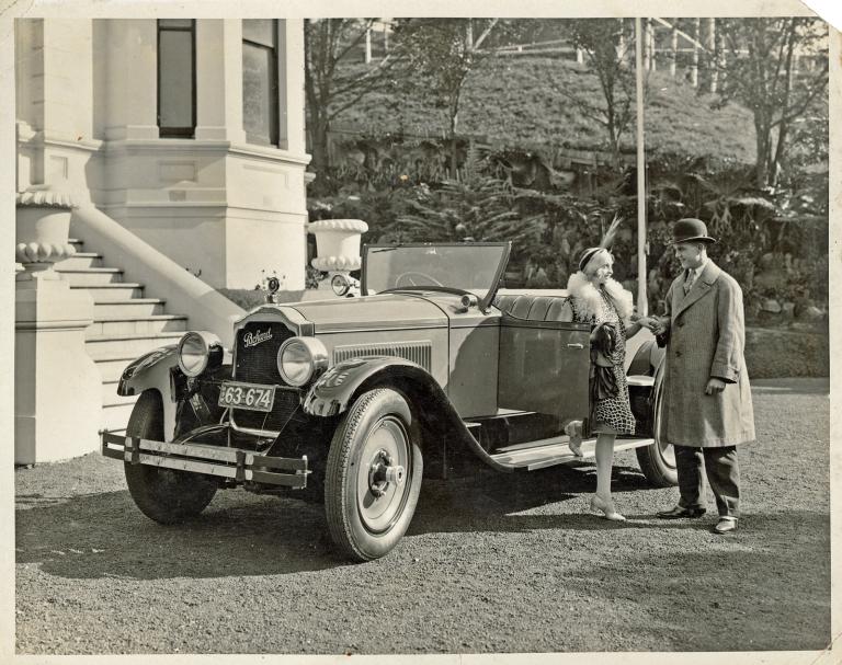A 1926 motor vehicle parked outside a mansion, a man and woman stand beside the car.