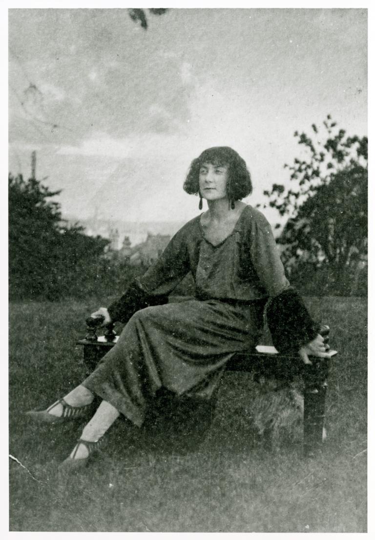 Silent era film director, Paulette McDonagh seated on an outdoor bench with her legs crossed.