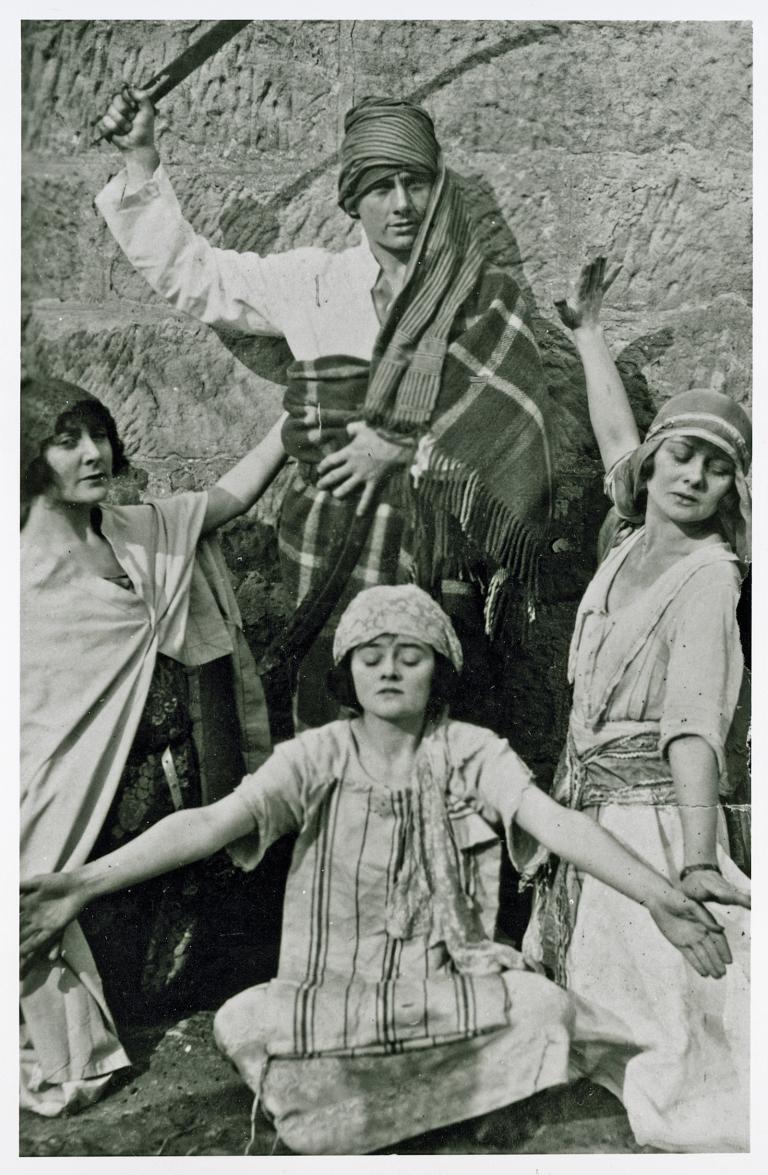 The McDonagh sisters wearing costumes and playacting on rocks, possibly on the Hawkesbury River, with their brother John who is also in costume wearing a turban on his head and holding a sword.
