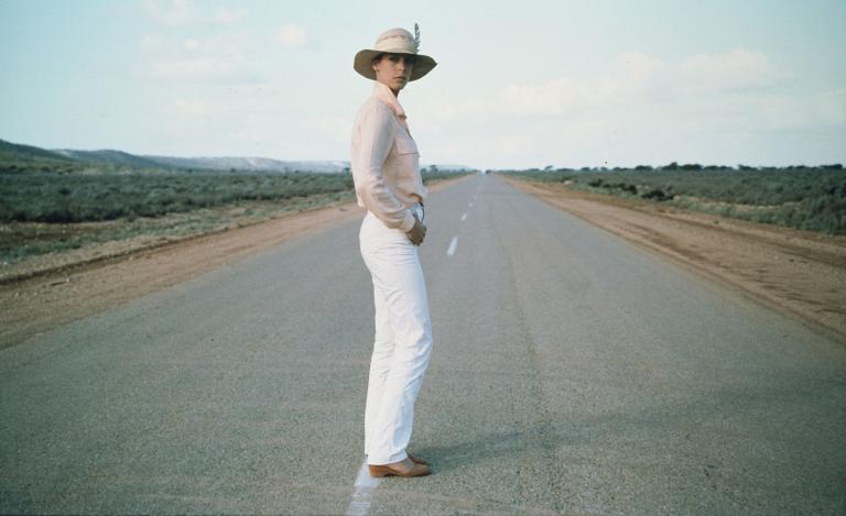 Jamie Lee Curtis dressed in white posing on a deserted outback highway in the movie Roadgames
