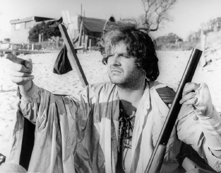 Hugh Keays-Byrne as Toecutter in Mad Max holding a rifle and pointing.