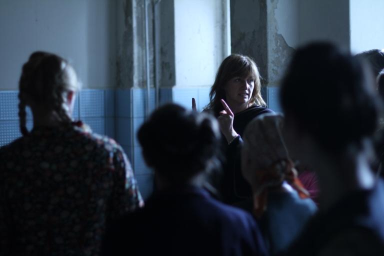 Director Cate Shortland directs a room full of people. We see the other people from behind and out of focus.