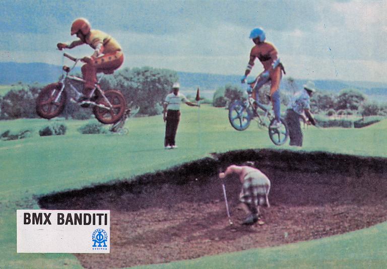 Two teens on BMX bikes jump across a sand trap in a golf course. The image is a lobby card promoting the film BMX Bandits (1983).