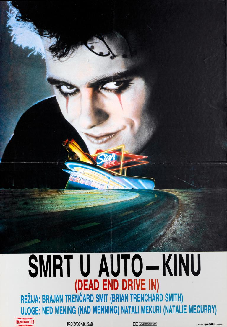 Close up of a menacing looking man with dark eye make up and an evil grin. His head looms over a smaller image of a neon-lit drive in cinema and empty road.