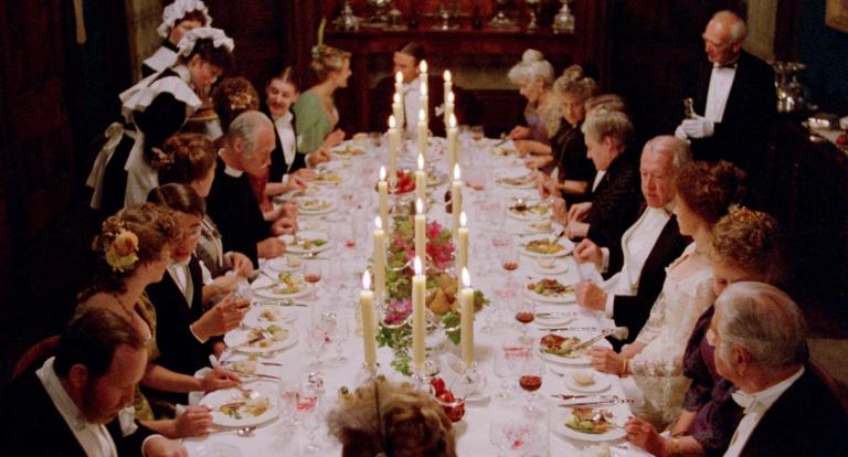 A large 1890s dinner party is in full swing as seated guests converse and eat while being served by maids and a butler in a scene from My Brilliant Career