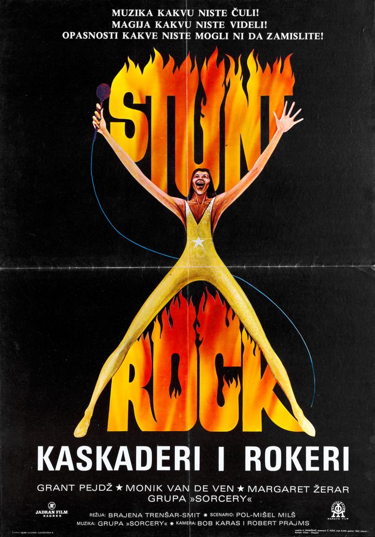 Poster art for film 'Stunt Rock'. A man in a yellow unitard with hands up and outstretched and a wide stance holding a microphone in one hand. The film title is made to look like flames written above his arms and between his legs on a black background.