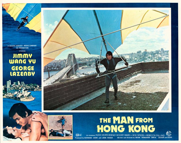Lobby card with main image of getting set to hang glide of a tall building. In the background you can see the Sydney Harbour Bridge and Sydney skyline. Around this image is the film title on blue background and other scenes from the film.