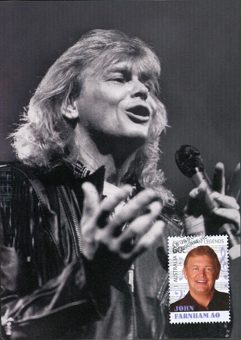 John Farnham pictured singing and holding a mic in his hand, circa 1987. There is an inset of a postage stamp in the bottom right corner which also has an image of Farnham on it.