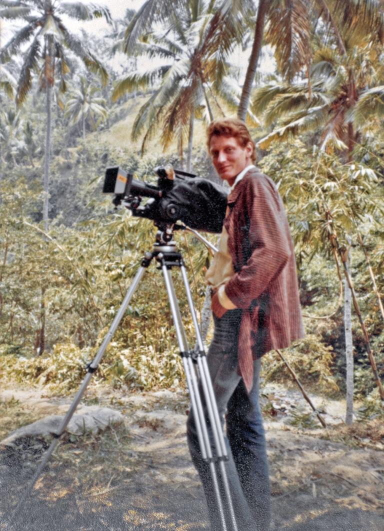 Australian documentary filmmaker John Darling standing next to camera on tripod in a jungle area in Bali