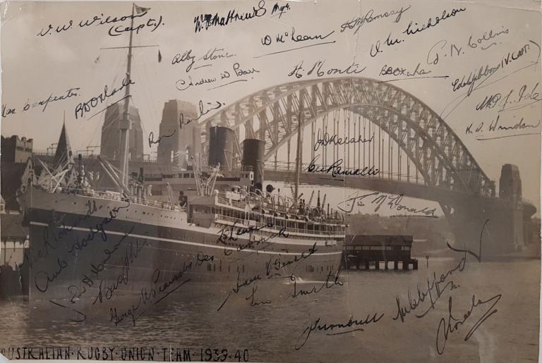 Photo of a ship in front of the Sydney Harbour Bridge. The photo has a lot of signatures on it. 
