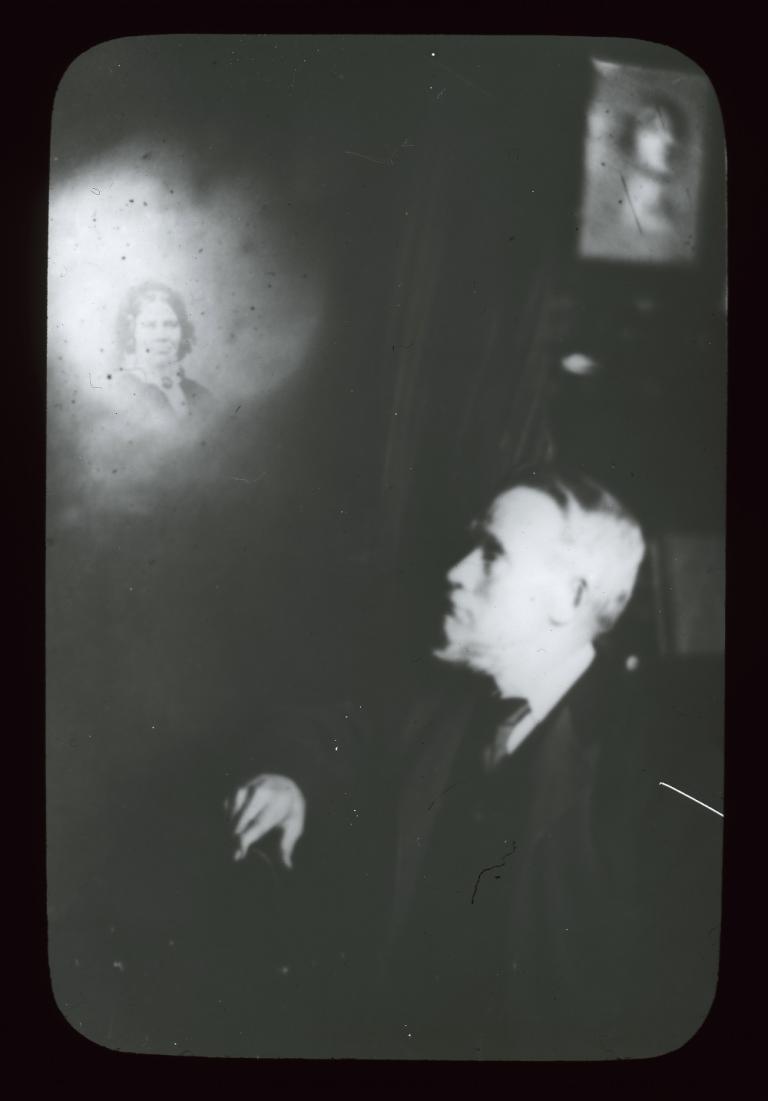 Black and white glass slide showing the upper body left profile of a man looking up to his right at an illuminated spirit.