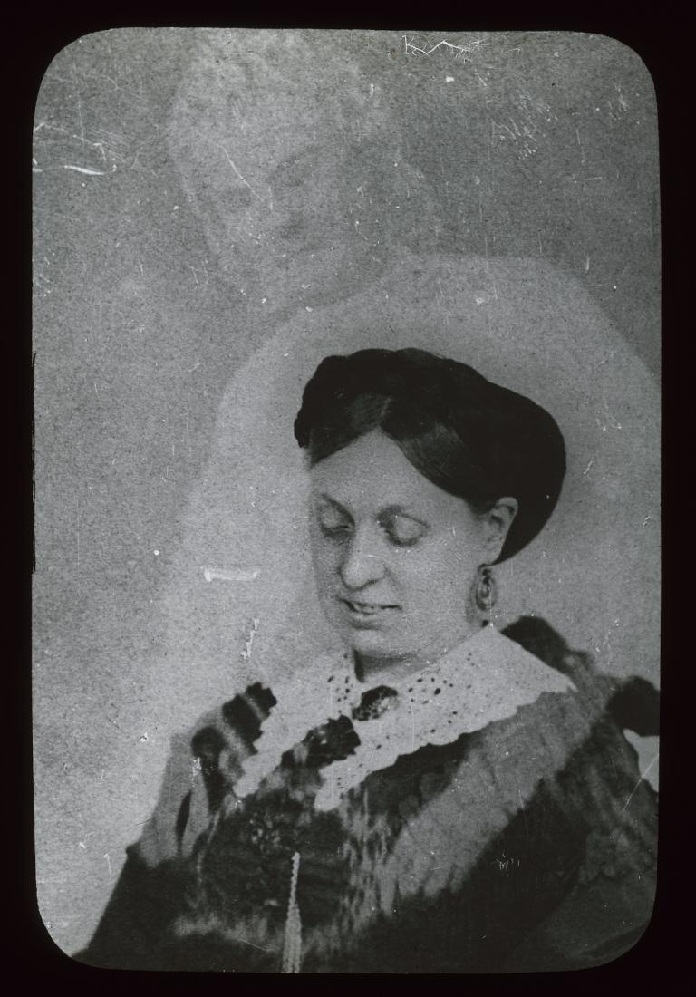 Black and white glass slide showing the upper body of a woman looking down, a spirit leaning over her, resting arms over her shoulders
