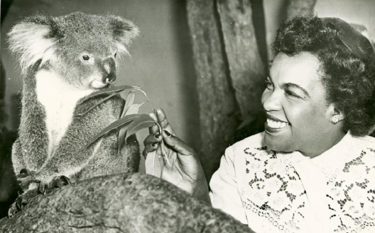 Winifred Atwell hands a gum leaf to a bemused looking Koala