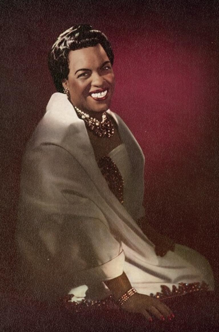 Coloured studio portrait of Winifred Atwell seated and smiling at the camera