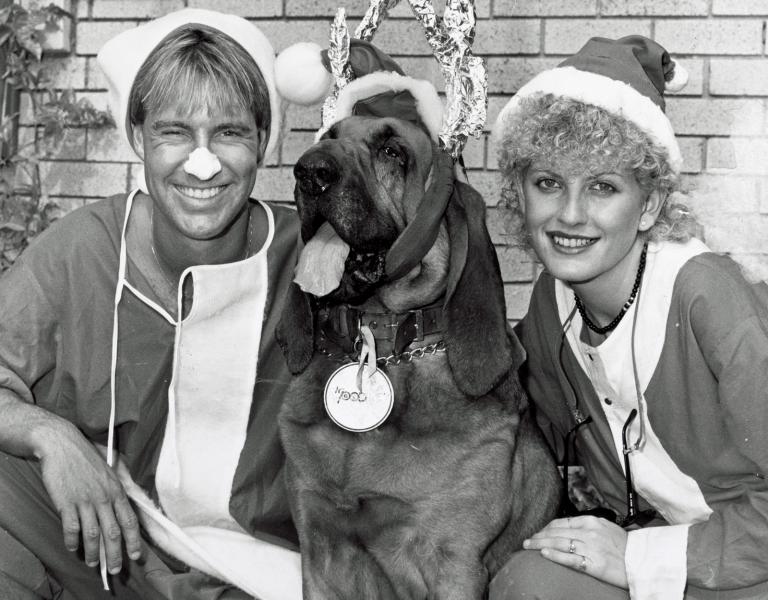 Brett Clements, Woodrow the Bloodhound and Edith Bliss. Brett and Edith are dressed in Santa suits and Woodrow is wearing reindeer antlers