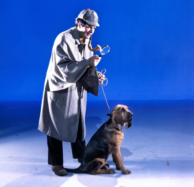 Simon Townsend and his dog Woodrow. Simon is dressed as Sherlock Holmes, with a pipe and magnifying glass and holding Woodrow's leash.
