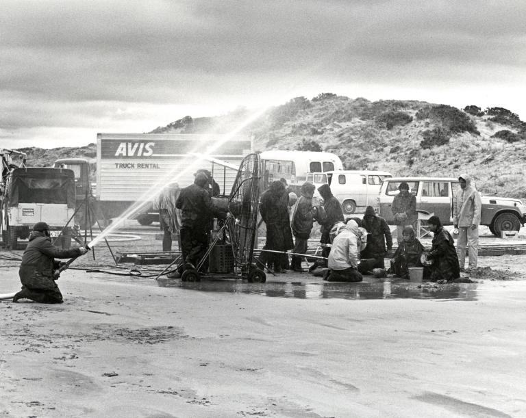 Scene during the shooting of Storm Boy, showing the crew 'making rain' with a hose connected to an off-camera water truck, a wind machine in the centre used to heighten storm effects, an Avis truck in the background which was used to haul heavy duty equip