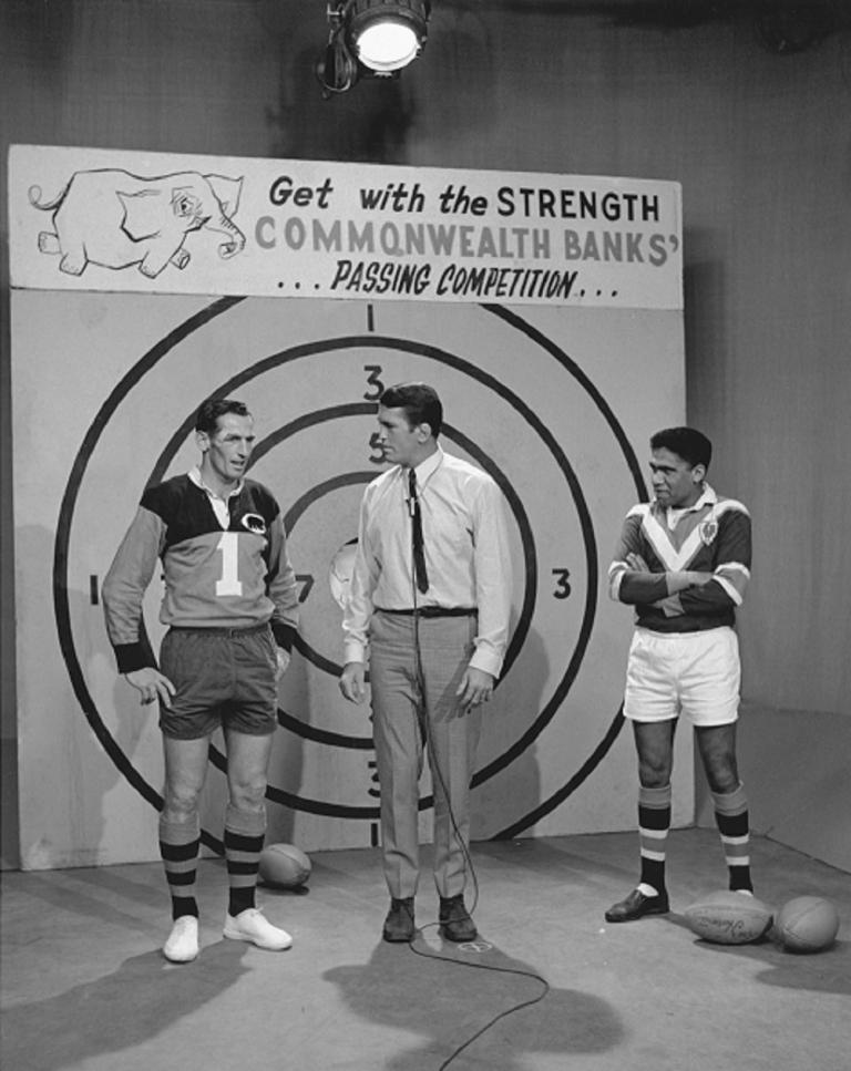 Black and white photo on set of The Rugby League Show with Rex Mossop centre, Ken Irvine to his right and Bruce Stewart on his left in front of the pass the ball competition taget.
