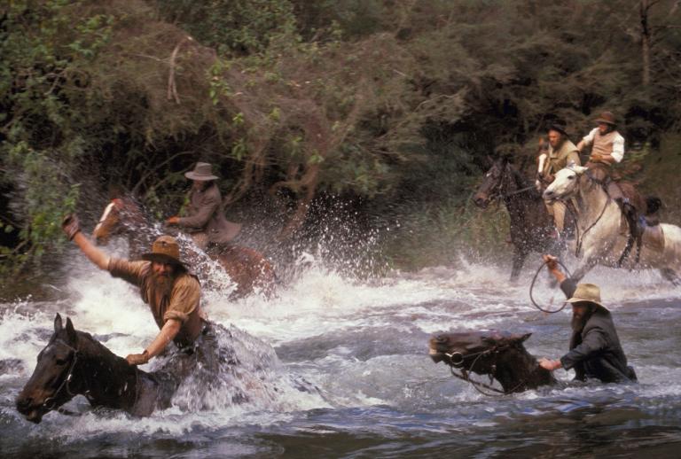 Men riding horses dash madly into a raging river