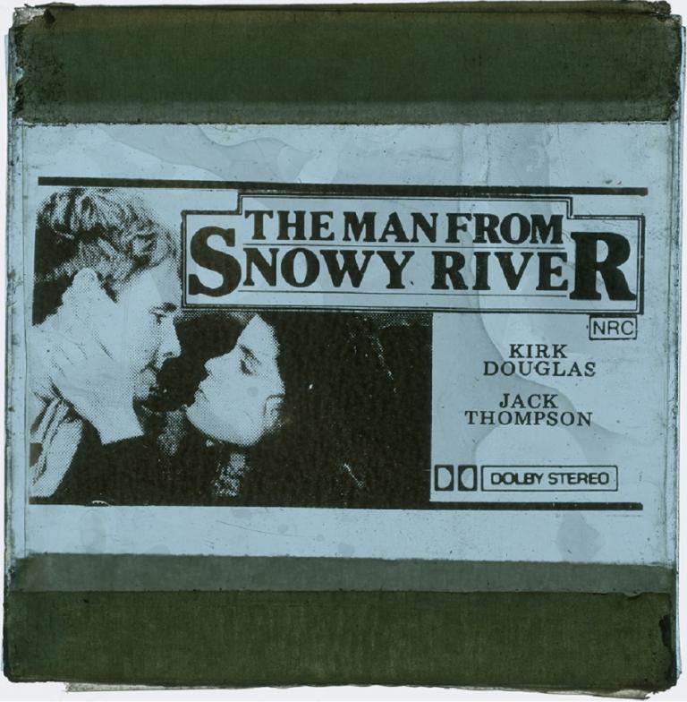Glass cinema slide comprising a blue background with 'The Man From Snowy River' written in black text and the two young stars about to kiss.