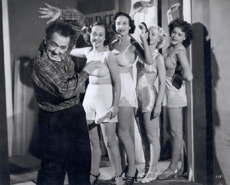 Four woman in underwear act as if to strike a cowering man.