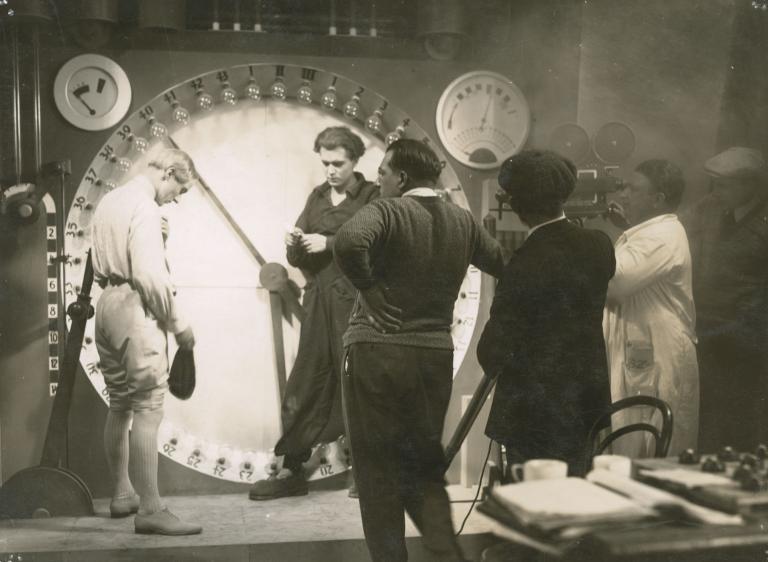 Fritz Lang directs two actors on a movie set while the cinematographer peers through the camera. Still from the making of the film Metropolis, 1927.