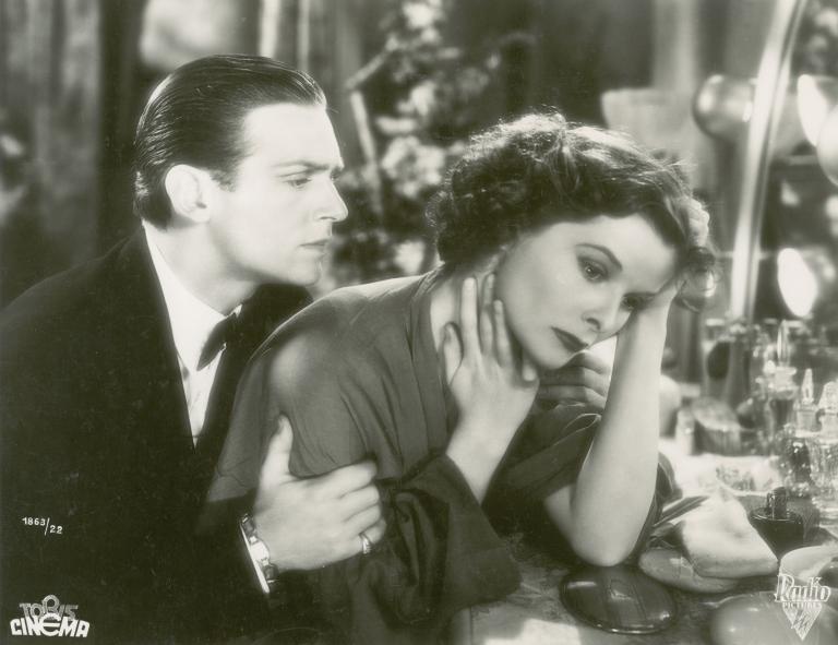 Douglas Fairbanks Jnr comforts Katharine Hepburn, who is seated at her dressing table, in a still from Morning Glory, 1933.