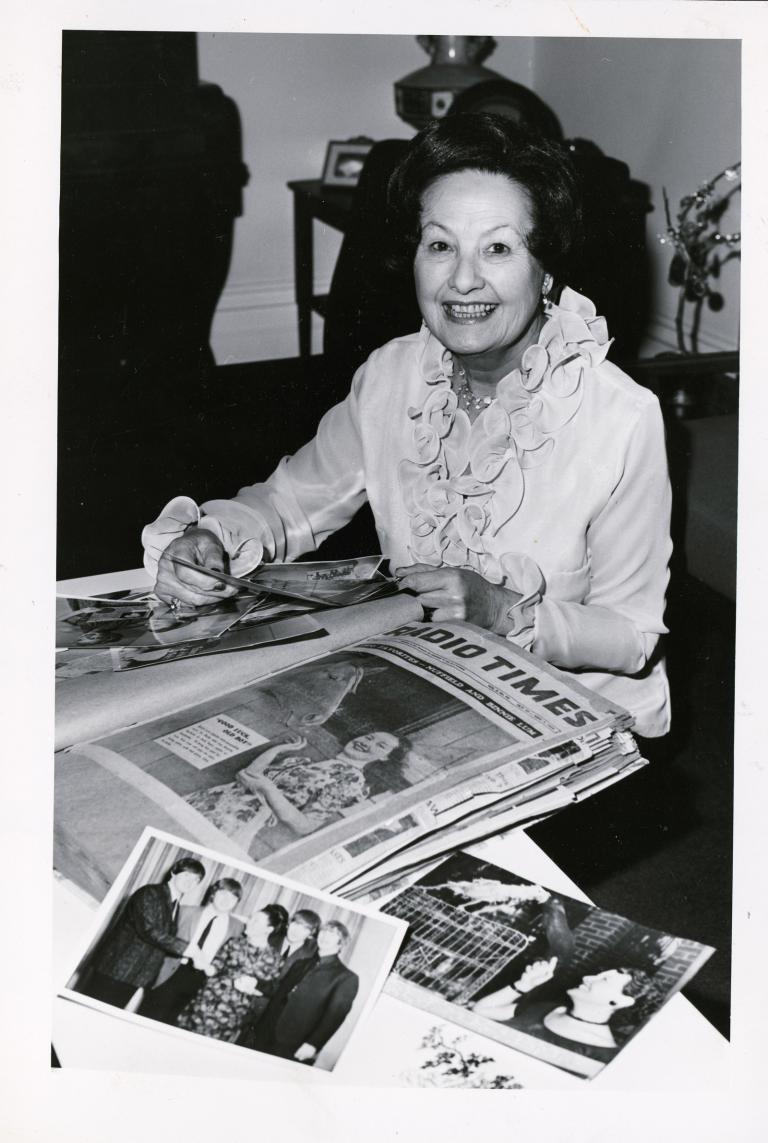 Binny Lum pictured at home, sitting at her desk with her scrapbook and surrounded by photos. 