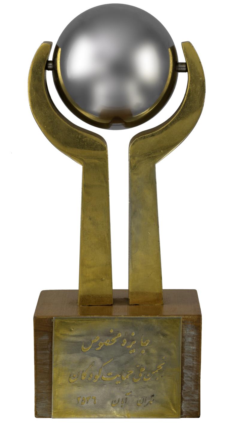 Chrome sphere suspended between two brass arms, mounted on wooden plinth. Gold coloured metal plaques are attached to opposite sides of the plinth.