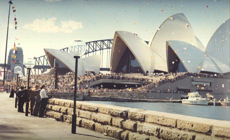 The Sydney Opera House as seen from the Botanical Gardens on its opening day. There are lots of people and colourful balloons. The Sydney Harbour Bridge is in the background