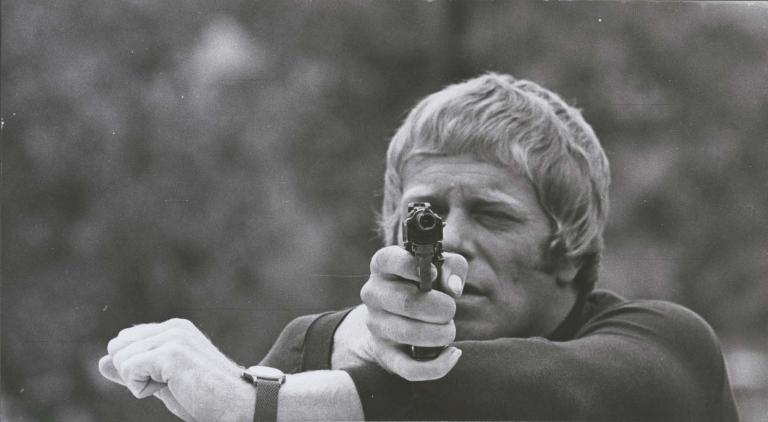 Jack Thompson points a gun at the camera in a 1970 episode of Australian detective TV show Homicide