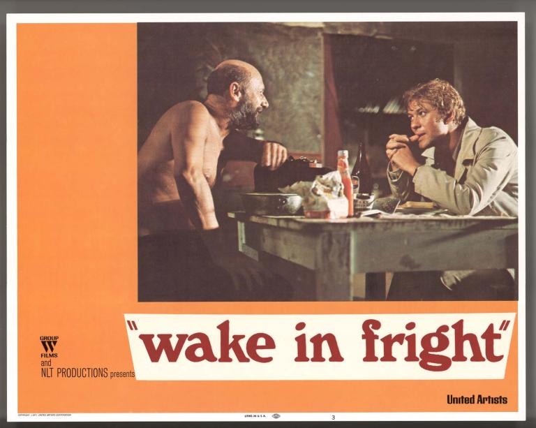 Wake in Fright film lobby card featuring a photo of Donald Pleasence and Gary Bond seated at a table in Doc's outback hut