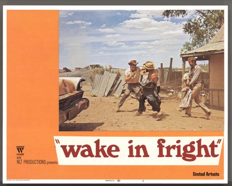 Wake in Fright film lobby card featuring a photo of Donald Pleasence and Jack Thompson play fighting in the dust, watched by Gary Bond