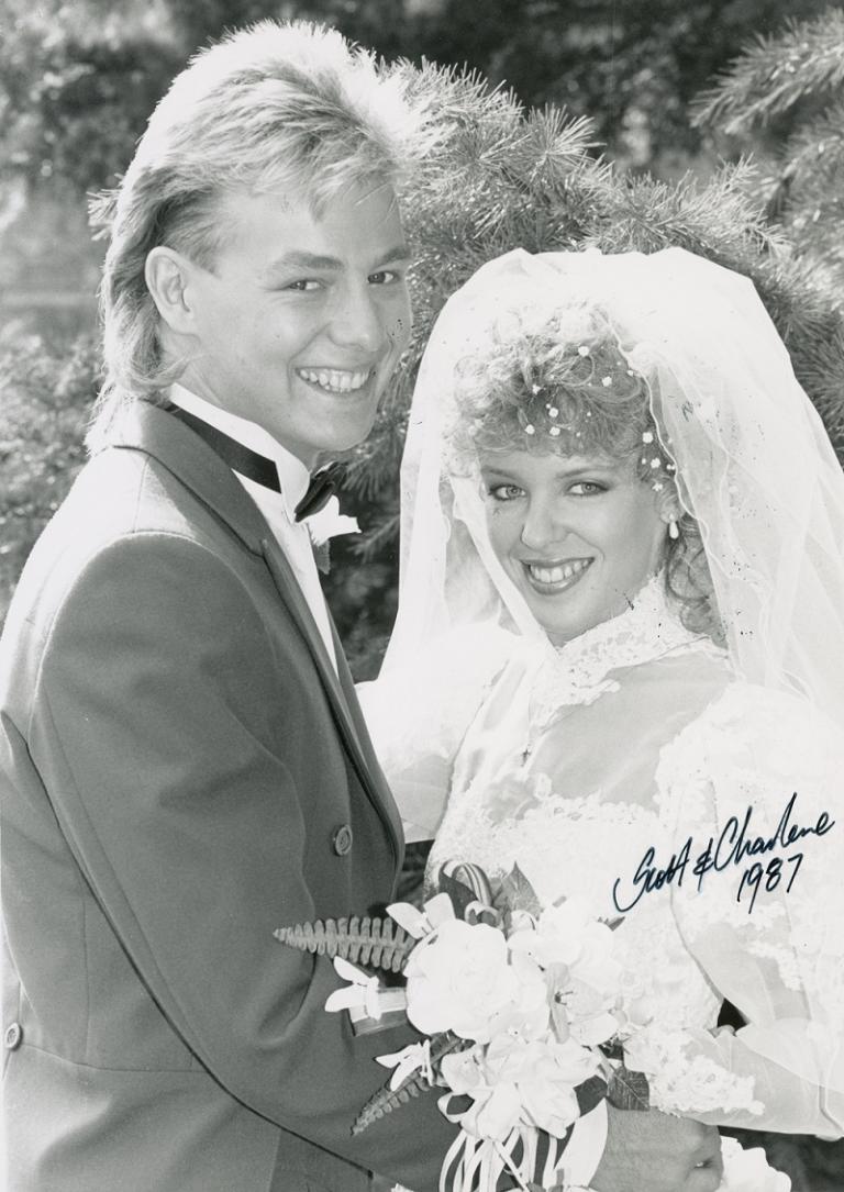 Scott and Charlene played by Jason Donovan and Kylie Minogue are all smiles on their wedding day. Charlene holds a bouquet of flowers. Handwritten text reads 'Scott and Charlene 1987'.