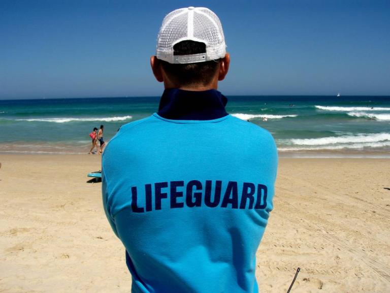 A lifeguard with his back to the camera watches over Bondi Beach in a scene from Bondi Rescue