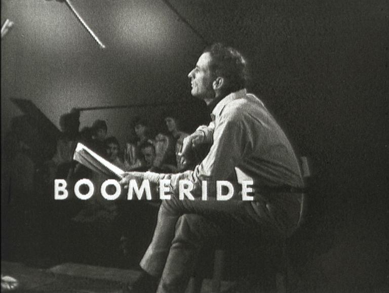 Australian singer/songwriter Charles Marawood pictured in profile sitting on a stool with legs crossed and playing a guitar. In the background there are some members of a live TV studio audience. The title 'Boomeride' is written across the centre.